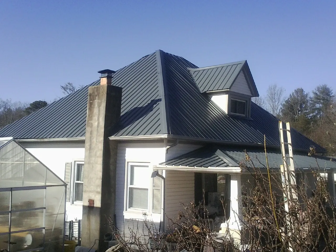 Dark blue standing seam metal roof on a white farmhouse with dormer — Slate & Tile Roof Repair by Roofing Brothers in Many