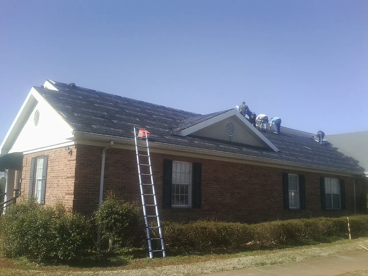 Crew tearing shingles off a brick ranch roof with a ladder set — Metal Roof Repair work by our crew in Many