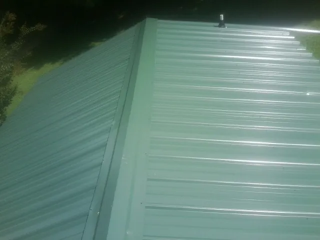 New green metal panels meeting at the ridge of a roof — Flat Roof Repair work by our crew in Many