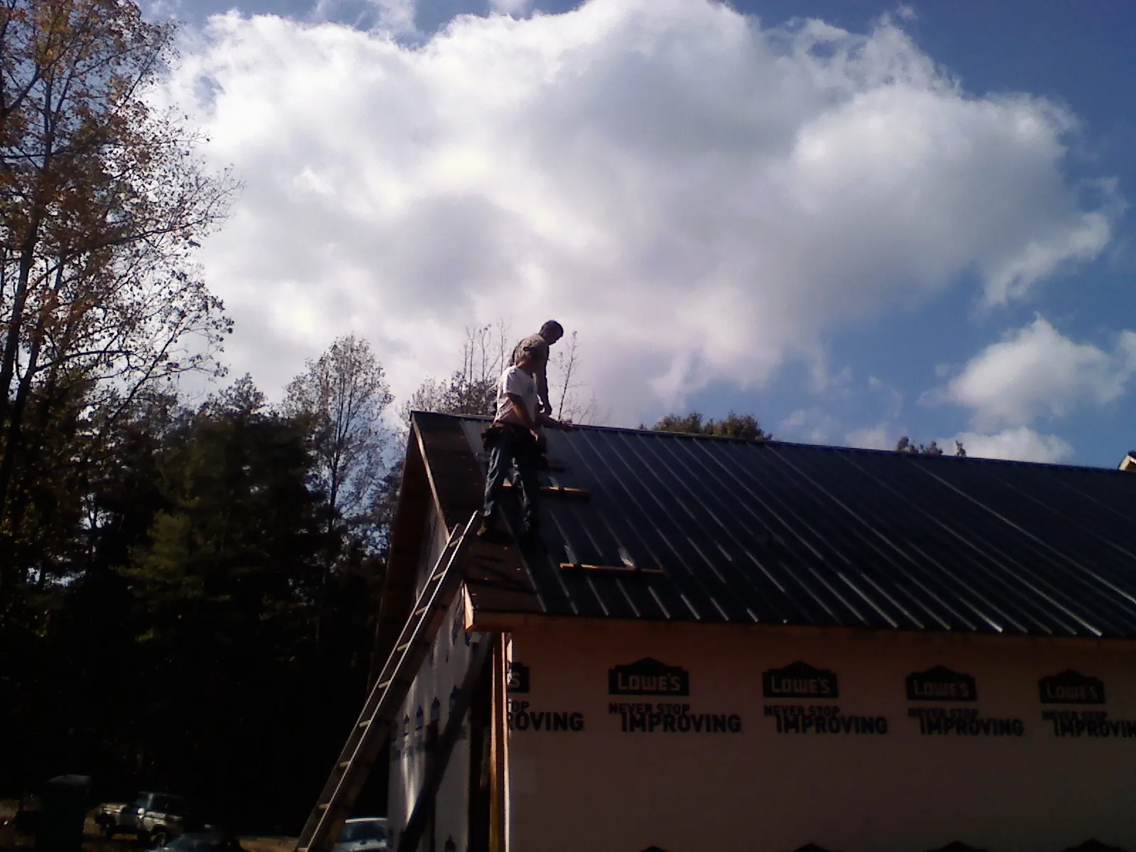 Roofer fastening dark metal panels high against a cloudy sky, from a Roof Inspection job in Many
